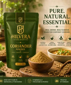 Hilvera pure coriander powder 100g pouch standing next to a wooden bowl filled with freshly ground dhaniya powder, whole coriander seeds, and a bowl of curry on a rustic wooden counter.